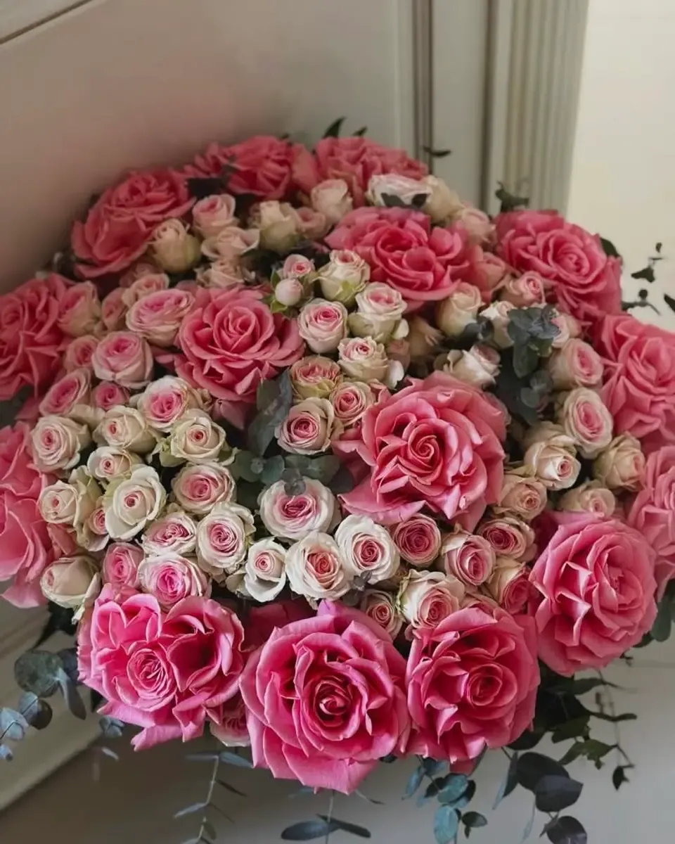 Bó hoa hồng hồng lớn tròn đầy, xen hoa hồng nhỏ trắng hồng và lá bạch đàn trong ánh sáng ấm