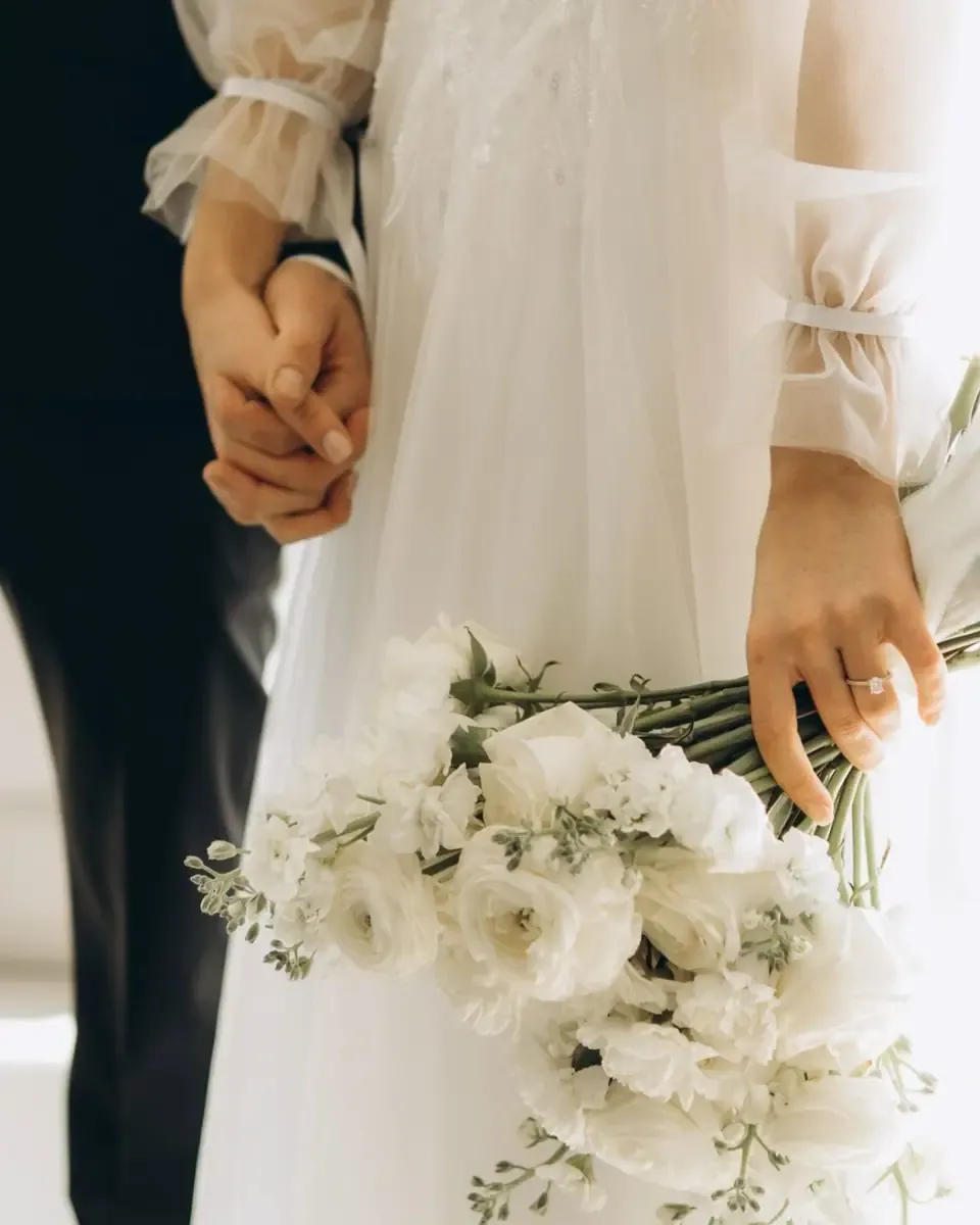 Bó hoa hồng trắng tròn dày cầm cạnh váy cưới đính ngọc trai sáng