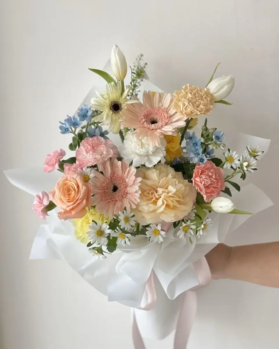 Bó hoa pastel hồng, cam, vàng nhạt và trắng gói giấy trắng, một tay cầm