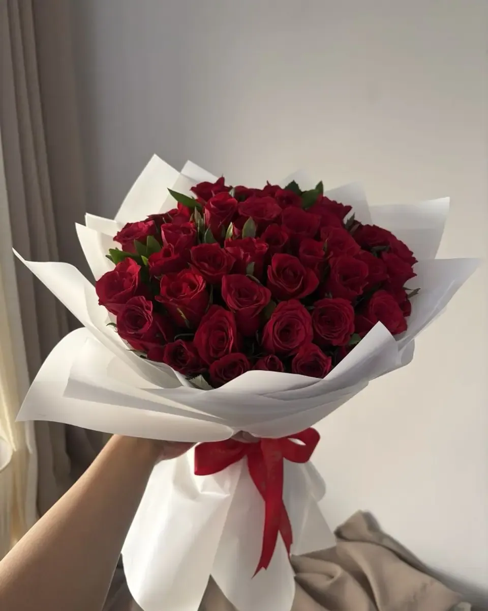 Bó hồng đỏ nhiều bông gói giấy trắng, ruy băng đỏ, cầm trên tay