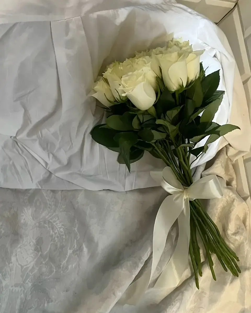 Bó hồng trắng buộc ruy băng kem đặt trên nền vải trắng