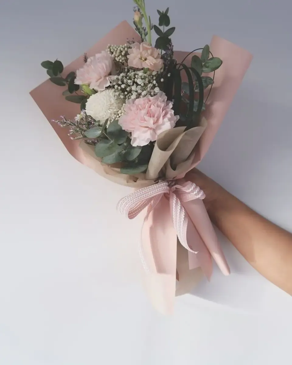 Bó hoa nhỏ có cẩm chướng hồng và hoa baby gói giấy hồng phấn, buộc ruy băng sọc