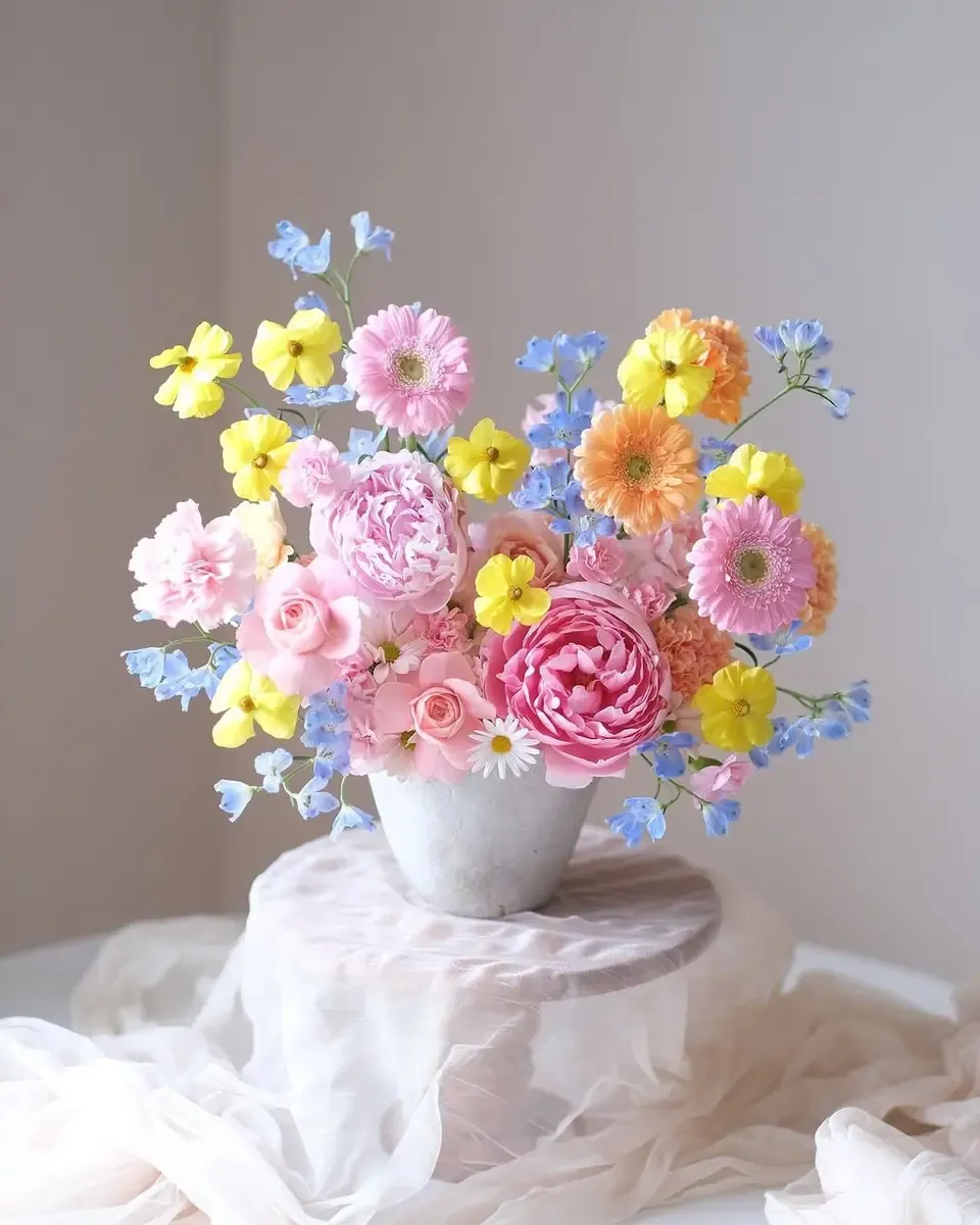 Bình gốm hồng cắm hoa tulip cam, cúc đồng tiền hồng, cúc trắng và cành nhỏ trên bục trắng