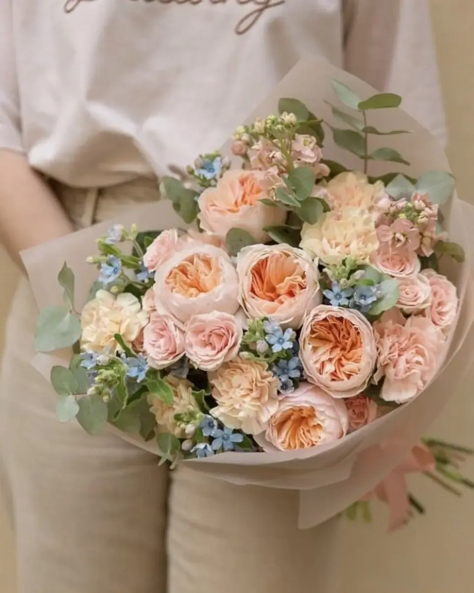 Bó hoa hồng đào, cẩm chướng và hoa nhỏ xanh, được ôm trước ngực người cầm