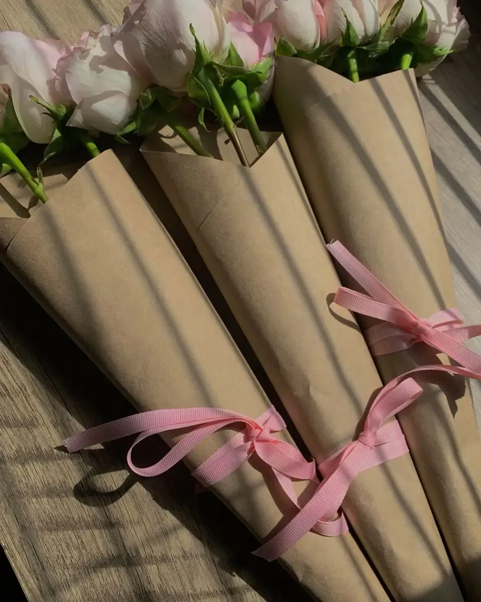 Những chiếc nón giấy kraft đựng hoa hồng, buộc ruy băng hồng, đặt dưới ánh nắng
