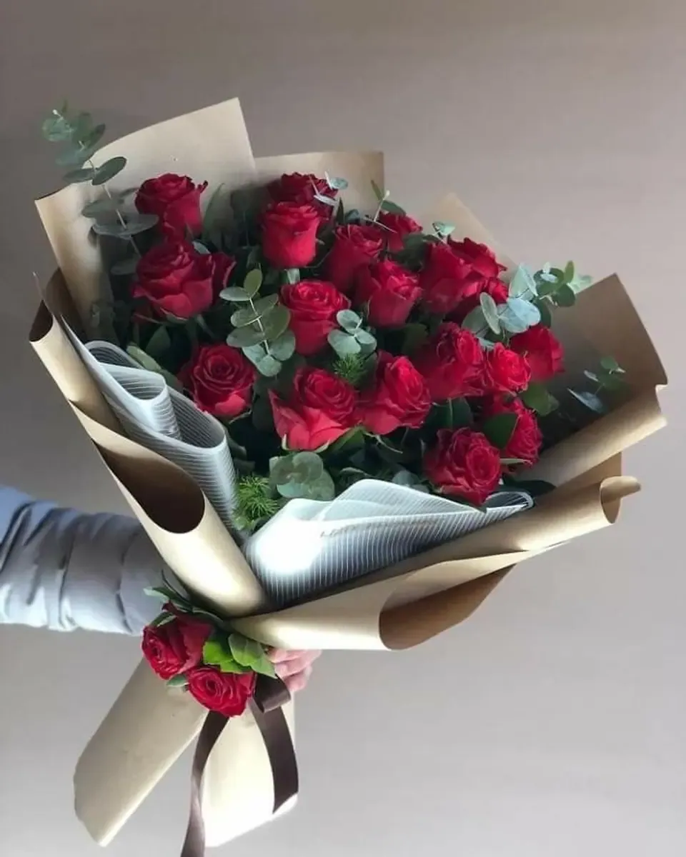 Bó hồng đỏ nhiều bông gói giấy kraft và giấy kẻ xám, một tay cầm