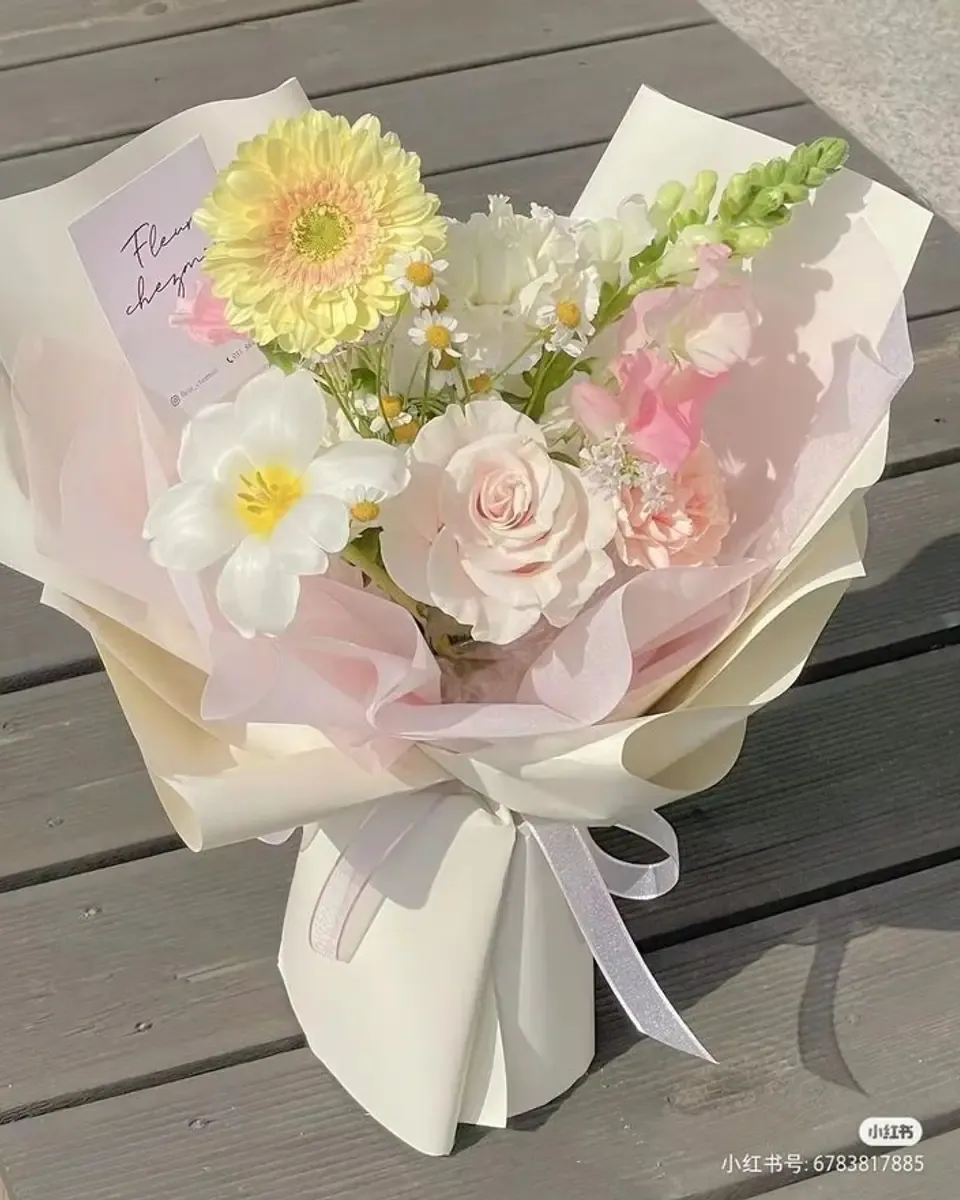 Bó hoa cúc đồng tiền, tulip trắng và hồng gói giấy trong hồng phấn, đặt trên sàn gỗ