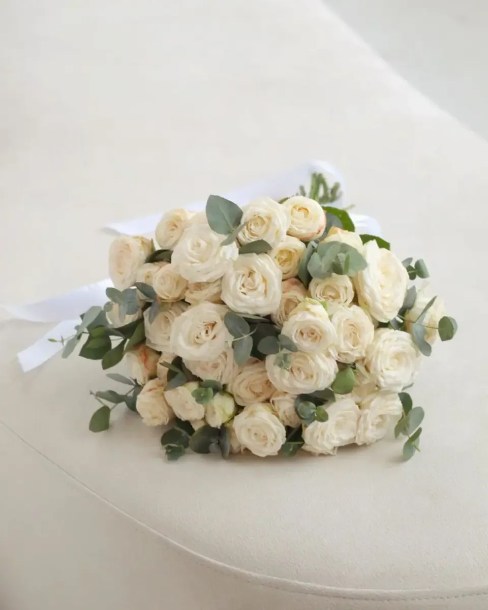 Bó hồng trắng kem nhỏ cùng lá bạch đàn đặt trên bàn sáng màu