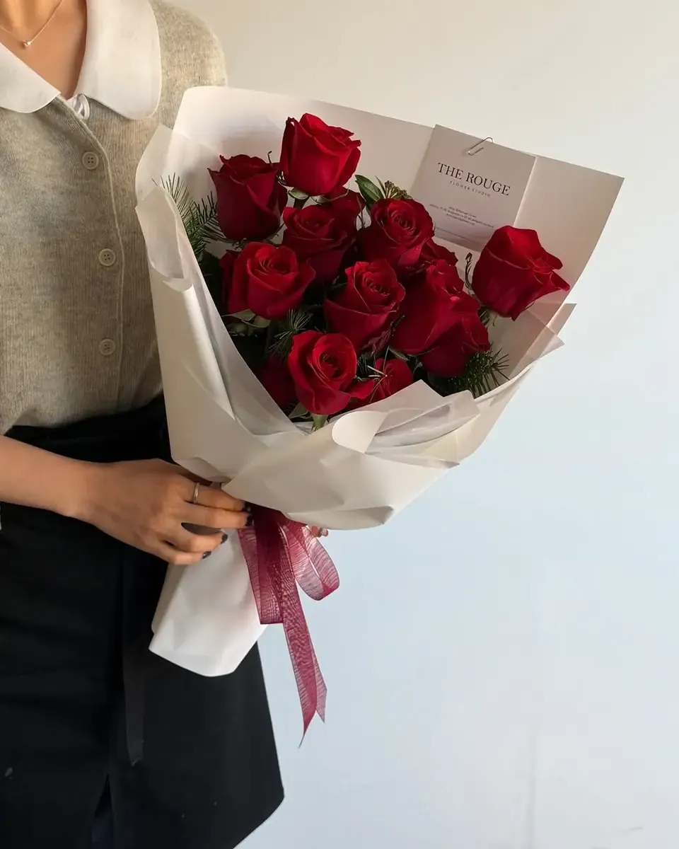 Bó hồng đỏ gói giấy trắng kem, ruy băng đỏ, người cầm mặc áo len khoác ngoài