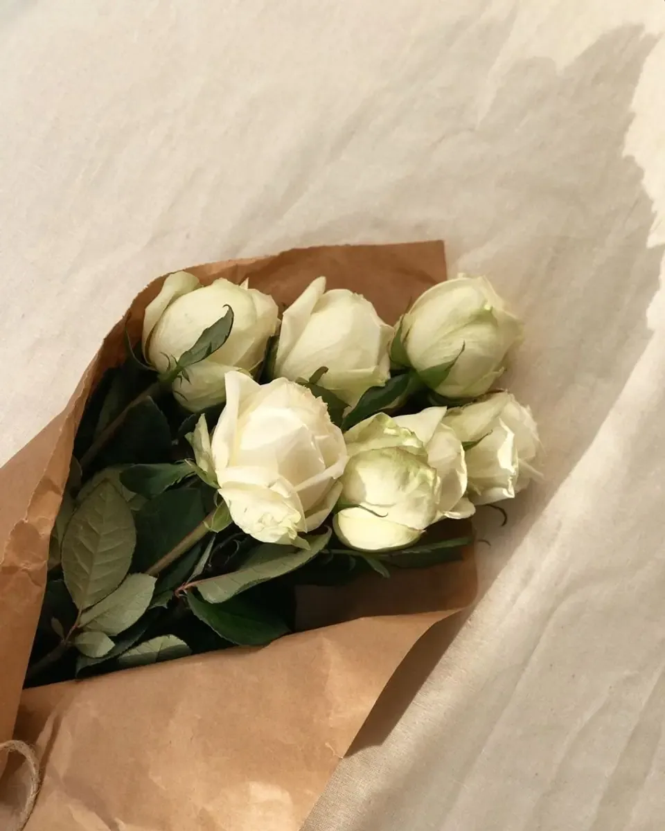 Bó hồng trắng gói giấy kraft đặt trên ga giường trắng