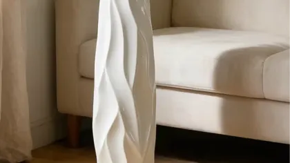 Bình trắng cao dáng uốn cắm cỏ lau, cành hoa trắng và lá bạch đàn cạnh ghế sofa kem