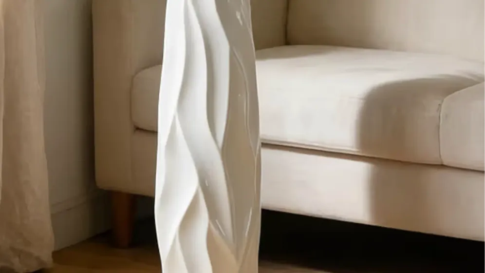 Bình trắng cao dáng uốn cắm cỏ lau, cành hoa trắng và lá bạch đàn cạnh ghế sofa kem