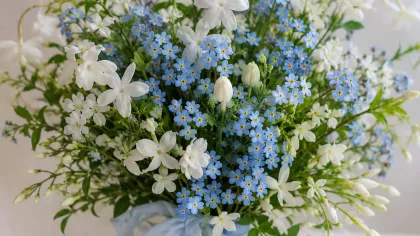 Bó hoa nhỏ màu xanh dương nhạt và hoa trắng buộc ruy băng xanh, đặt trên nền vải trắng