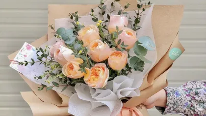 Bó hồng cam đào xen lá bạch đàn gói giấy kraft và giấy kem, buộc ruy băng cam, một tay cầm