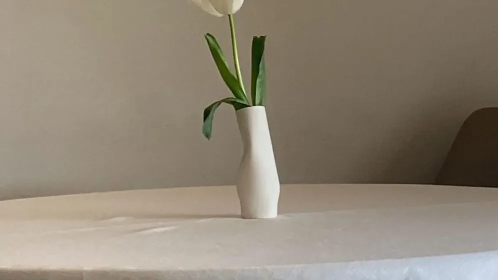 Một cành tulip trắng cắm trong bình sứ nhỏ màu kem đặt trên bàn tròn phủ khăn sáng