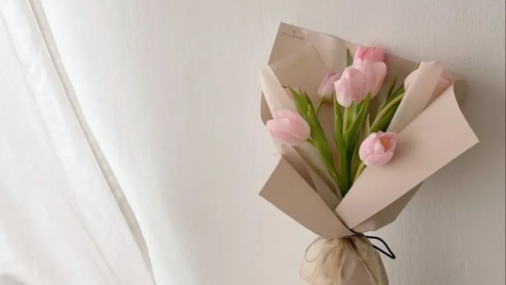Bó tulip hồng nhạt bọc giấy màu be đặt cạnh rèm voan trắng