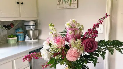 Bình hoa hồng hồng, hoa thạch thảo và dương xỉ đặt trên mặt bàn gỗ trong bếp sáng