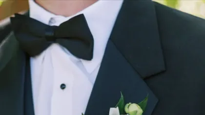 Hoa cài áo ranunculus trắng với lá xanh trên ve áo vest xanh đen và nơ đen
