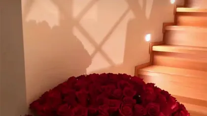 Bó hoa hồng đỏ rất lớn buộc dây đỏ đặt dưới chân cầu thang gỗ sáng ấm