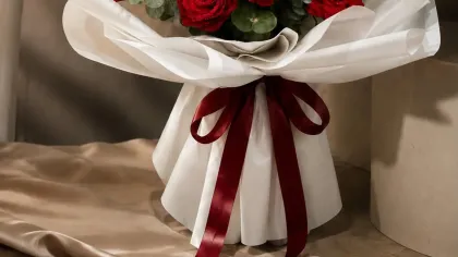 Bó hồng đỏ đầy đặn gói giấy trắng, ruy băng đỏ thẫm đặt trên bàn