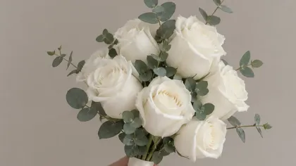 Bàn tay cầm bó hoa hồng trắng kèm lá bạch đàn xanh bạc trên nền xám sáng