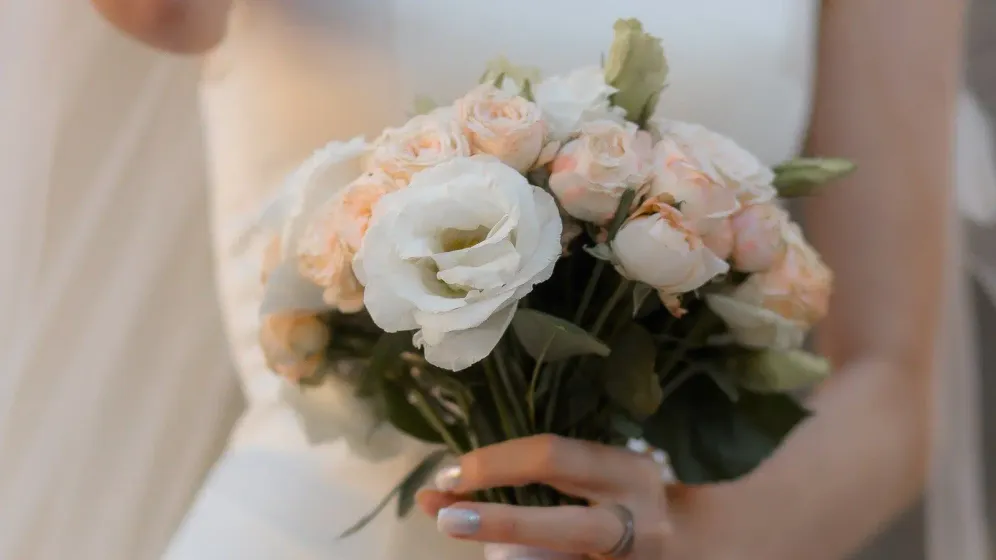 Cô dâu váy cưới trắng nhiều lớp cầm bó hoa hồng kem và hoa lisianthus trắng