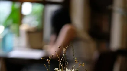 Bình thủy tinh nhỏ cắm vài cành hoa li ti đặt trên mặt bàn gỗ sẫm, nền mờ