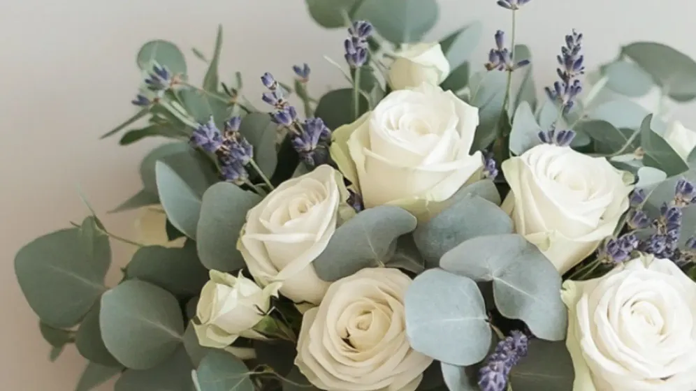 Bó hoa cưới tròn gồm hoa hồng kem, lá bạch đàn và hoa oải hương buộc ruy băng kem trên nền xám nhạt