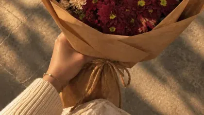 Bó cúc hồng đào và đỏ đô gói giấy kraft nâu, cầm trên đường nắng chiều