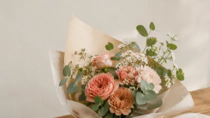 Bó hoa tông cam đào gói giấy kraft kem, buộc ruy băng hồng đất, đặt trên tấm vải lanh