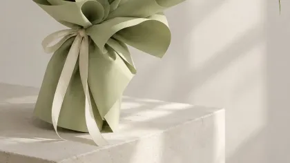 Bó tulip trắng cùng hoa xanh nhạt gói giấy xanh sage, buộc ruy băng kem, đặt trên bục sáng