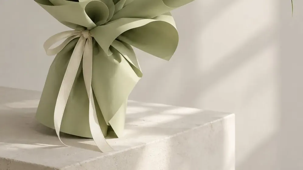 Bó tulip trắng cùng hoa xanh nhạt gói giấy xanh sage, buộc ruy băng kem, đặt trên bục sáng