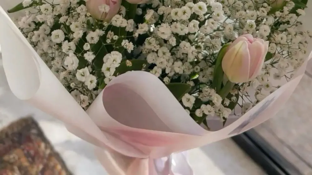 Bó tulip hồng nhạt cùng baby trắng gói giấy trắng, đặt bên khung cửa sổ