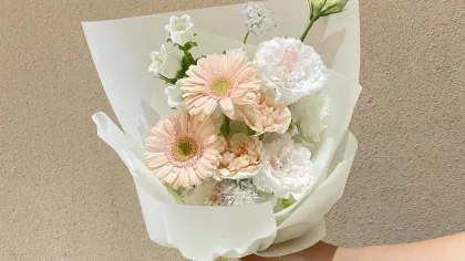 Bó hoa nhỏ tông kem, hồng đào gói giấy trắng, buộc ruy băng be, một tay cầm
