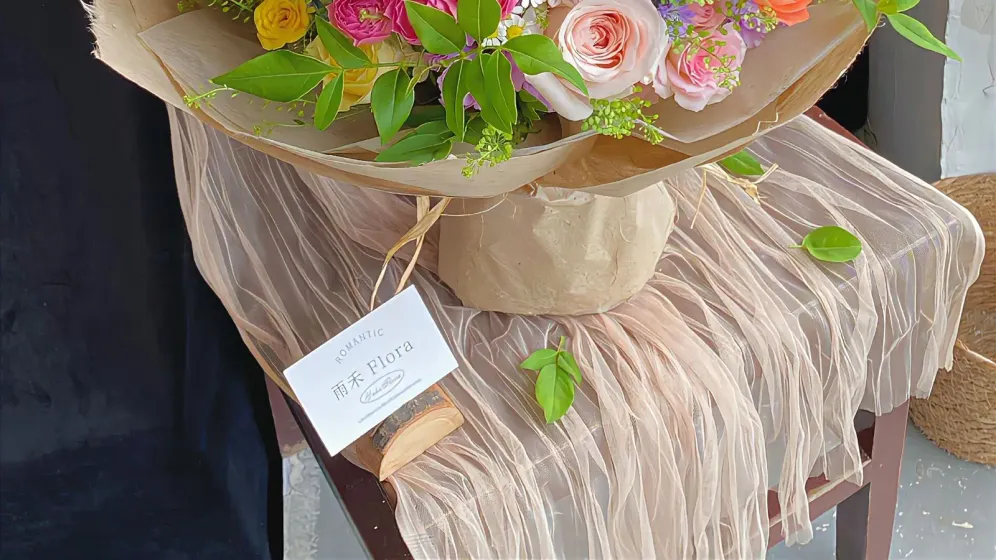 Bó hoa nhiều màu cam, hồng, vàng và tím nhạt gói giấy kem đặt trên ghế