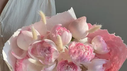 Bó sen hồng nhiều lớp cánh gói giấy hồng nhạt, buộc dây thừng, đặt trên bàn gỗ