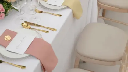 Bàn tiệc dài trải khăn trắng với hàng hoa nhiều màu pastel chạy giữa bàn, khăn ăn hồng và vàng nhạt